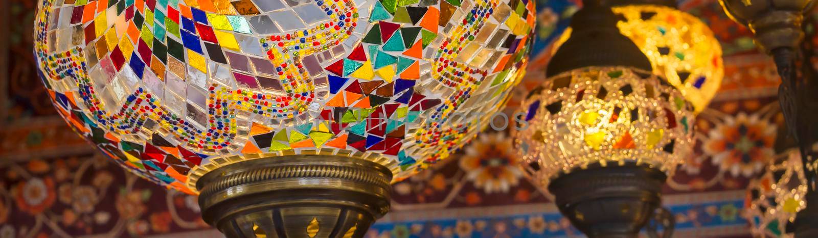 Middle Eastern lambas of different colors and sizes are hanging in the bazaar. Bright traditional Arabic and Turkish lanterns made of metal and glass, inlaid with mosaic details of different colors.