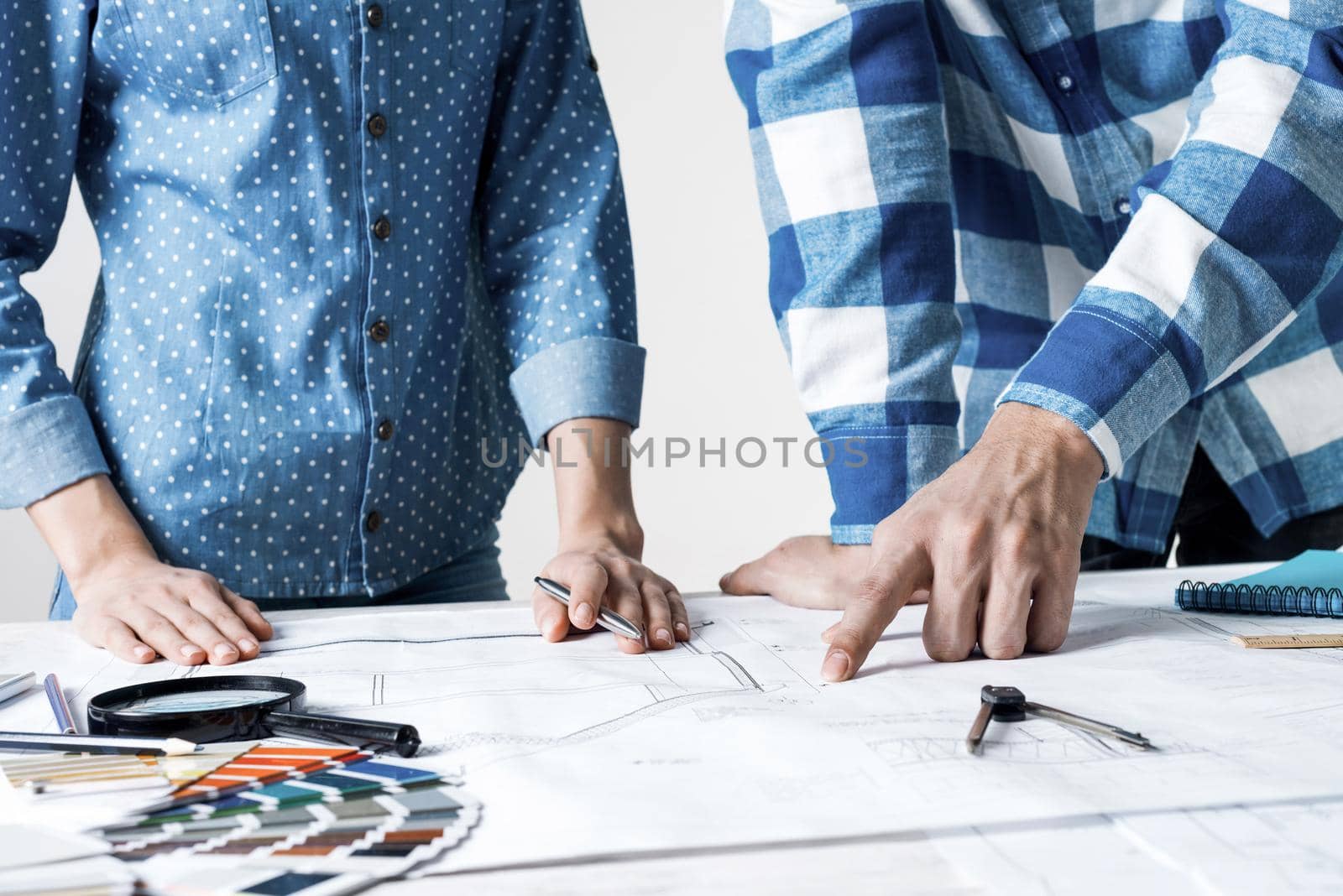 Man and woman together working at design project. Creative teamwork at workspace with construction blueprint and color swatches. People standing near desk and discussing in architecture studio.