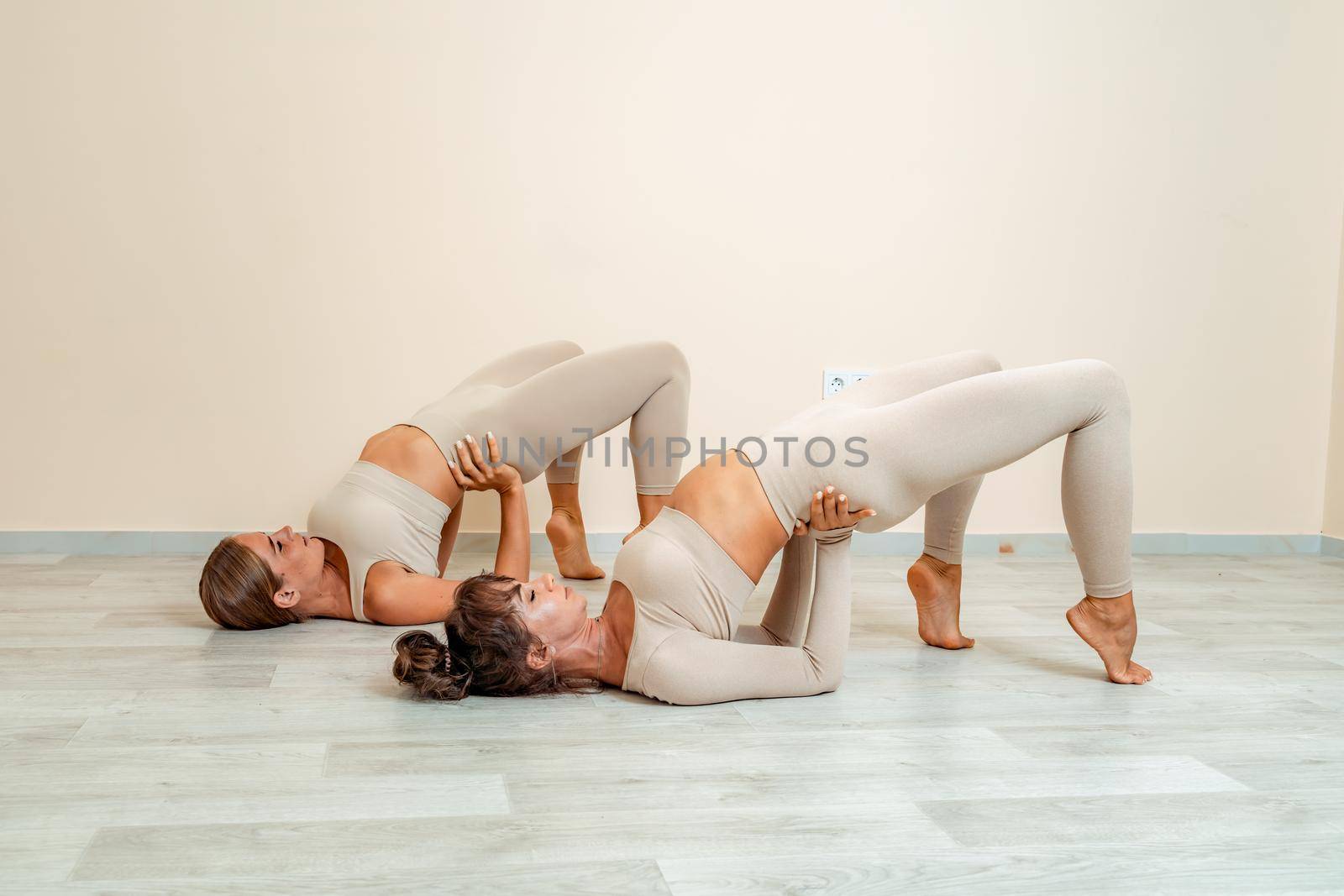 Fitness, pilates stretching exercises, a group of two attractive smiling mature women in beige sports clothes, train in a sports club. by Matiunina