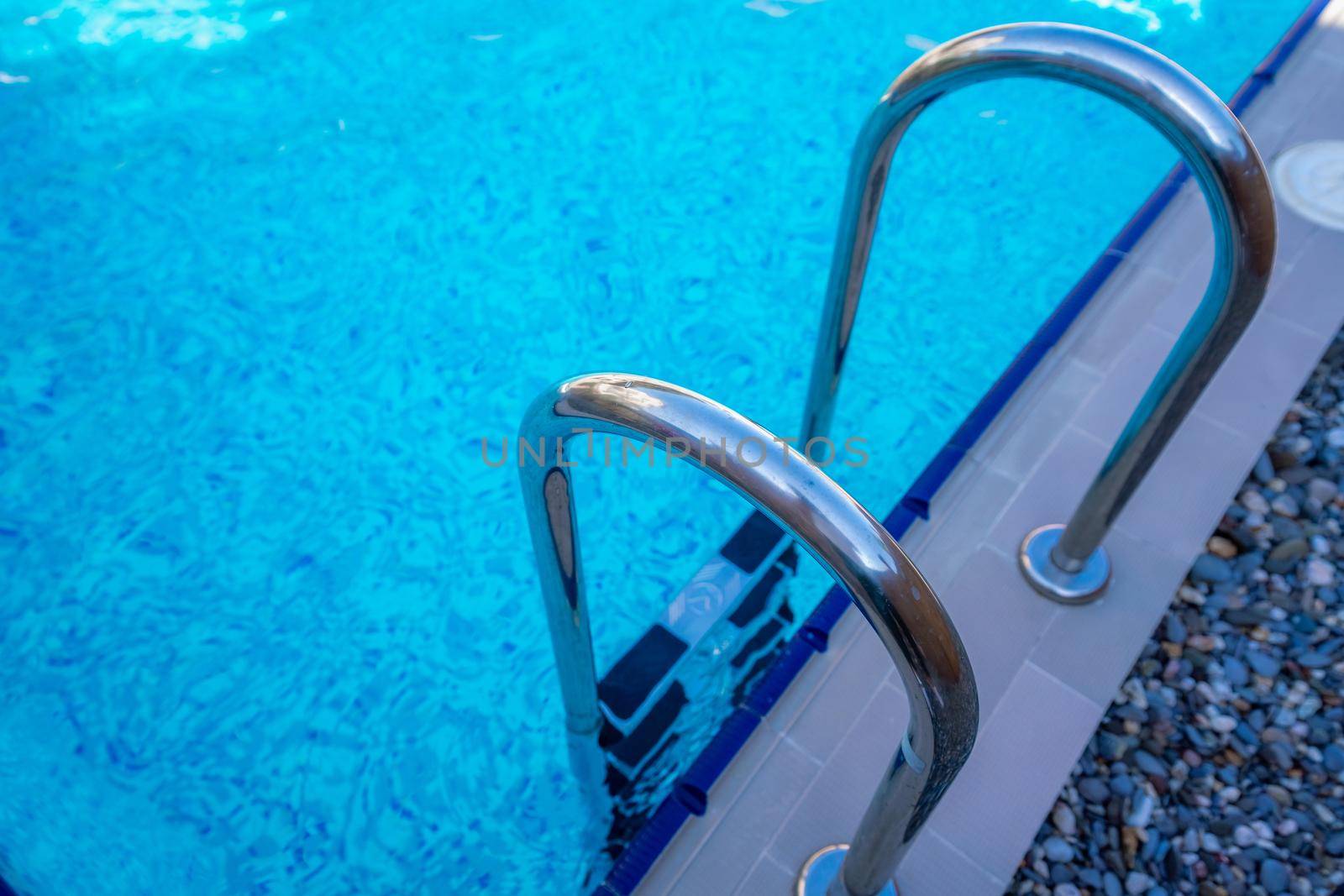 Background of blue transparent water in the swimming pool on the territory of the hotel. Descent to the pool with handrails. Rest and relaxation concept. Active rest by the sea.