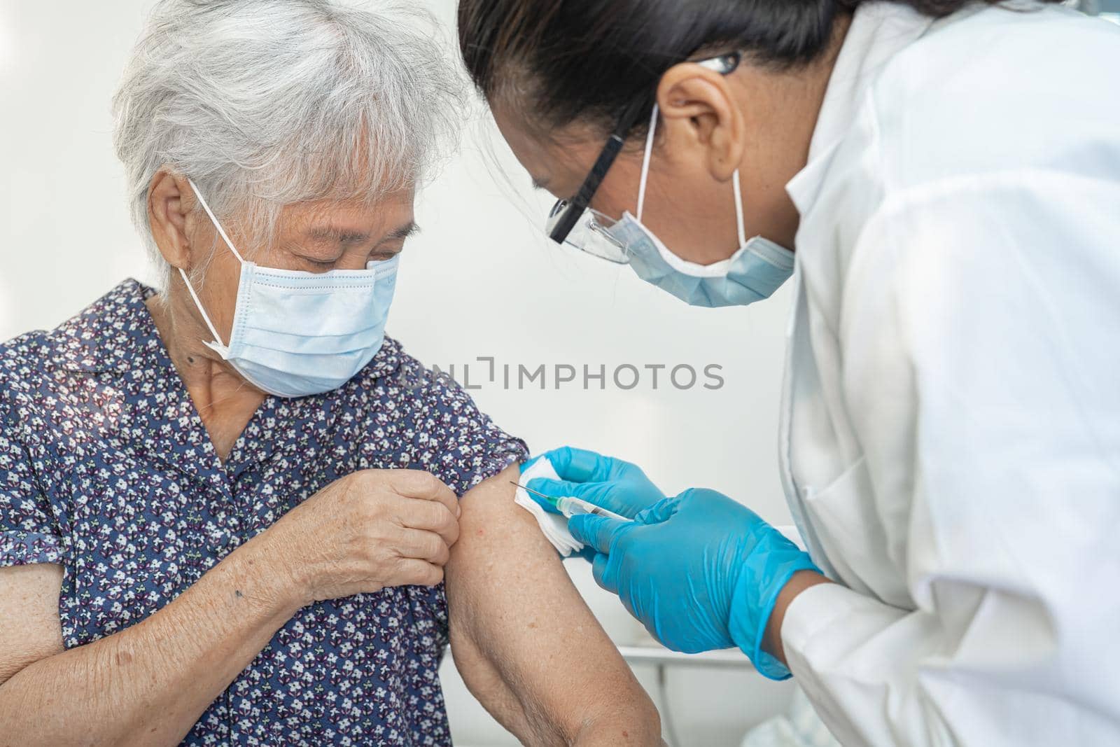 Elderly Asian senior woman wearing face mask getting covid-19 or coronavirus vaccine by doctor make injection. by pamai