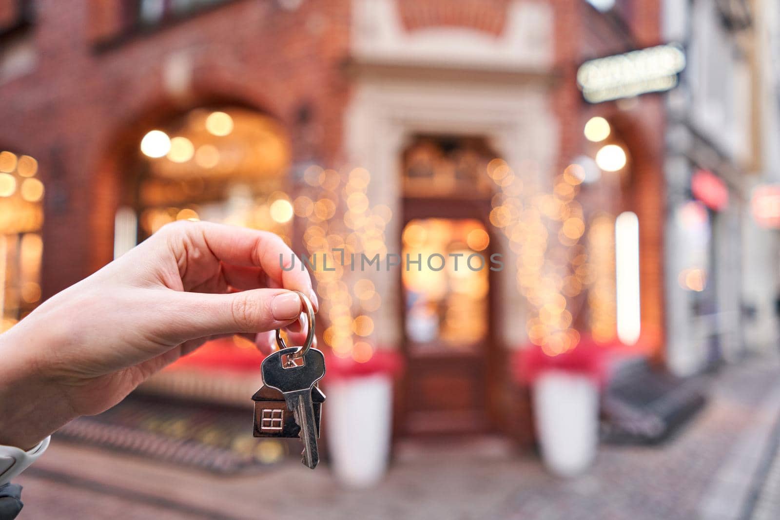 Mortgage or rent concept. Woman holding key with wooden house keychain . Real estate, hypothec, moving home or renting property. Christmas mood in blurred background.