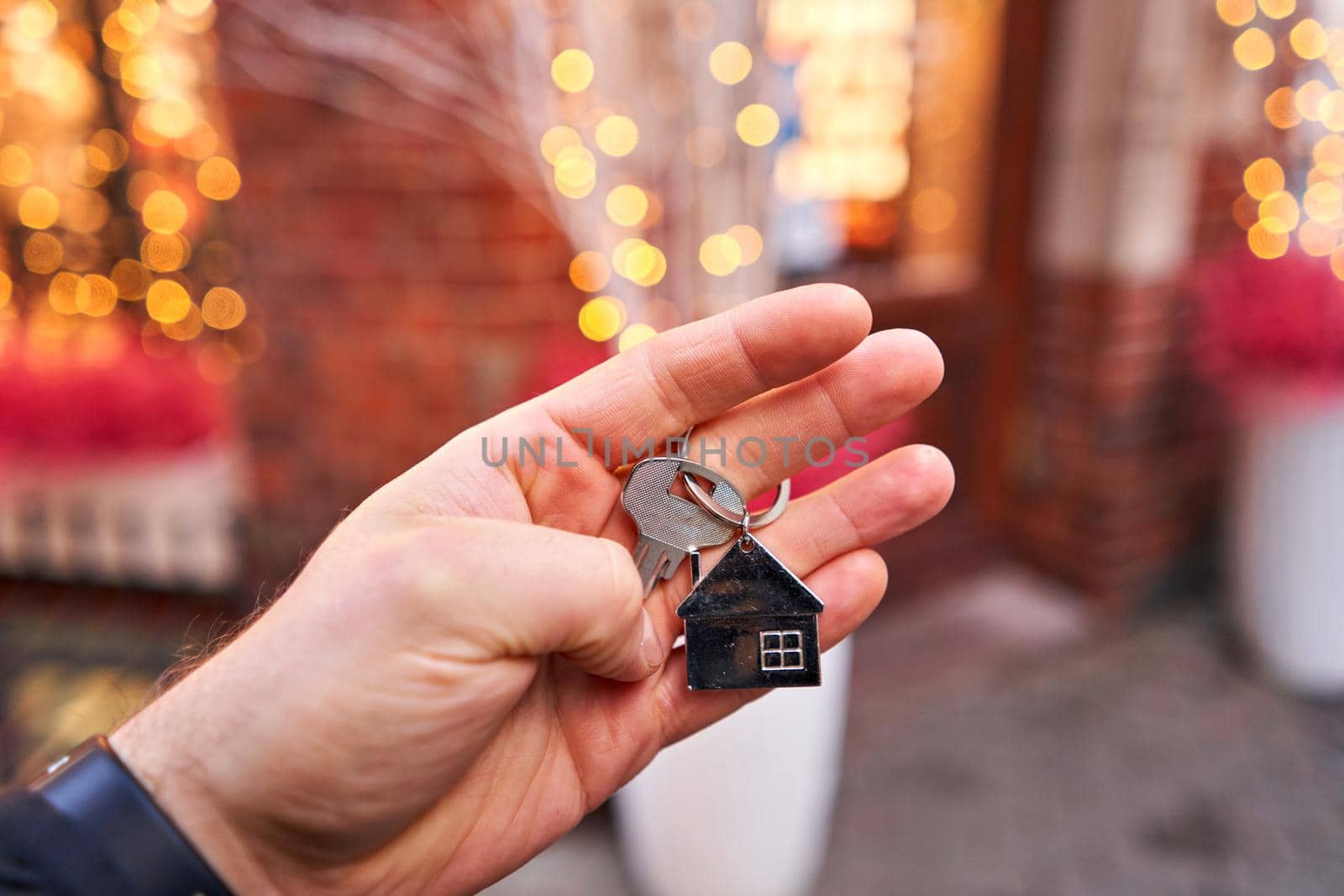 Rent a house for Christmas. Mortgage or rent concept. Man holding key with wooden house keychain . Real estate, hypothec, moving home or renting property. Christmas mood in blurred background