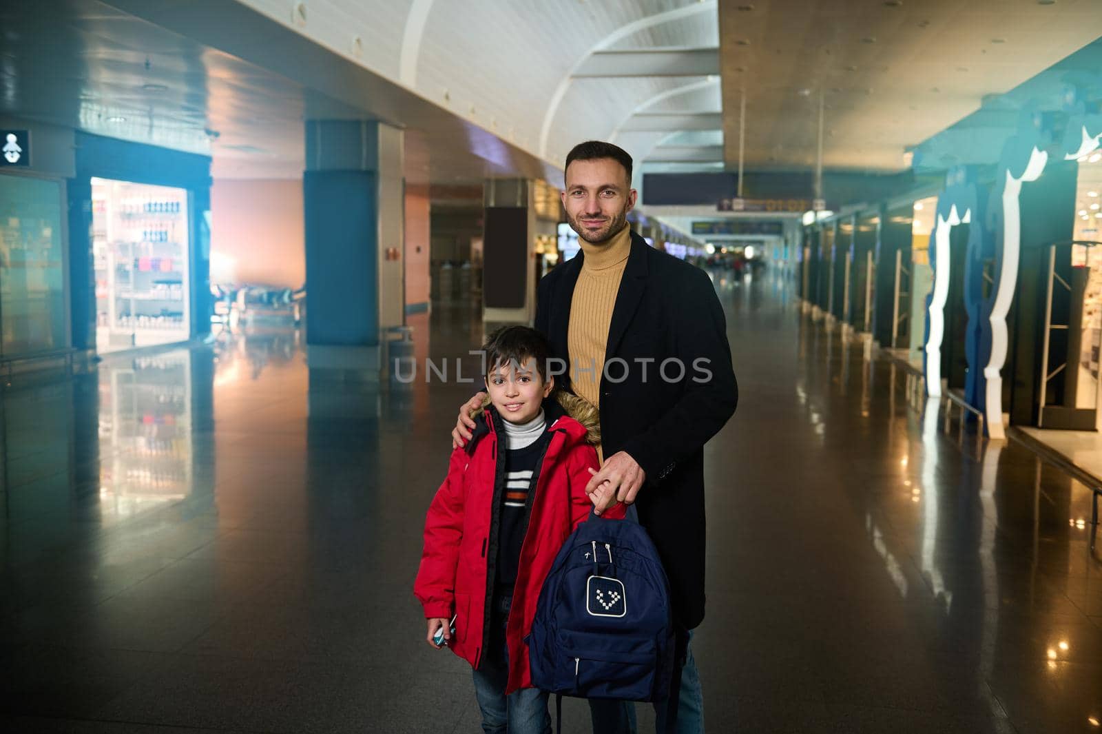 Handsome Caucasian man, young father travelling with his teenage son, standing together in the duty free shopping areas of the departure terminal of international airport