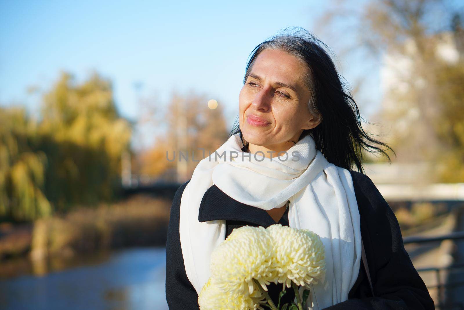 A beautiful middle-aged woman getting grey-haired in a dark coat in a spring town with a bouquet of flowers