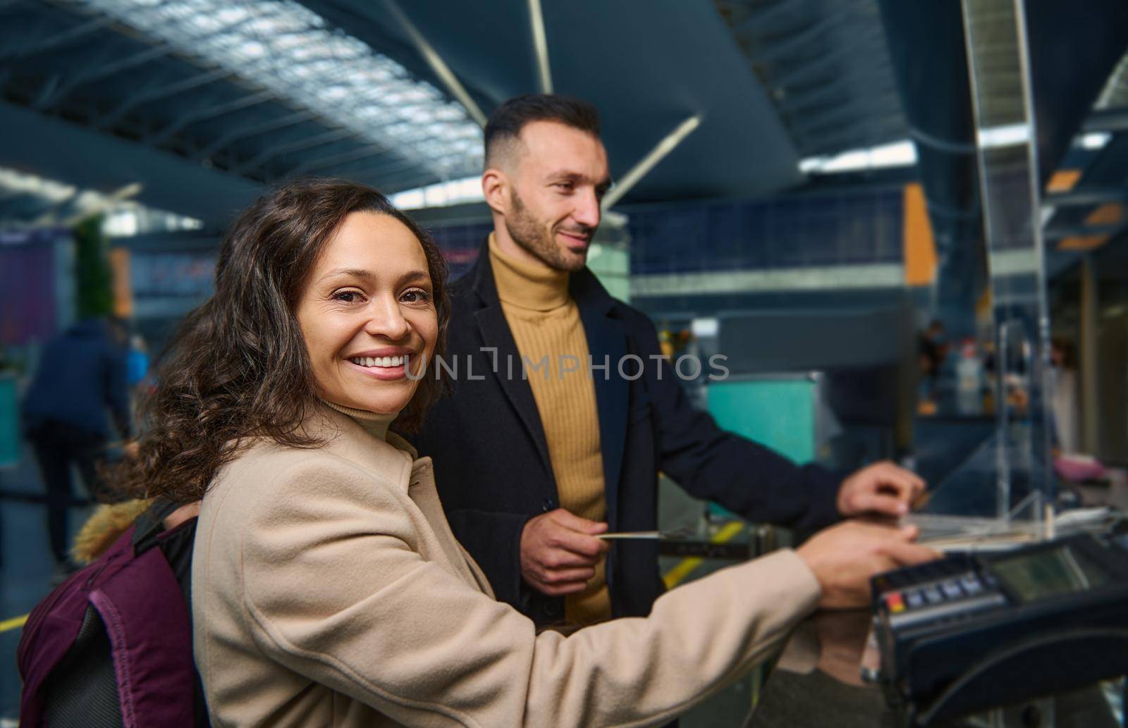 Beautiful middle aged ethnic couple - woman of Middle Eastern descent and handsome Caucasian man holding out passports while going through passport and customs control at international airport by artgf