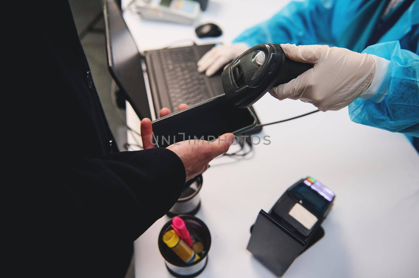 Close-up of a medical health care worker in protective clothing using scanner checking information from a mobile application on a smartphone phone about a traveler's health at international airport