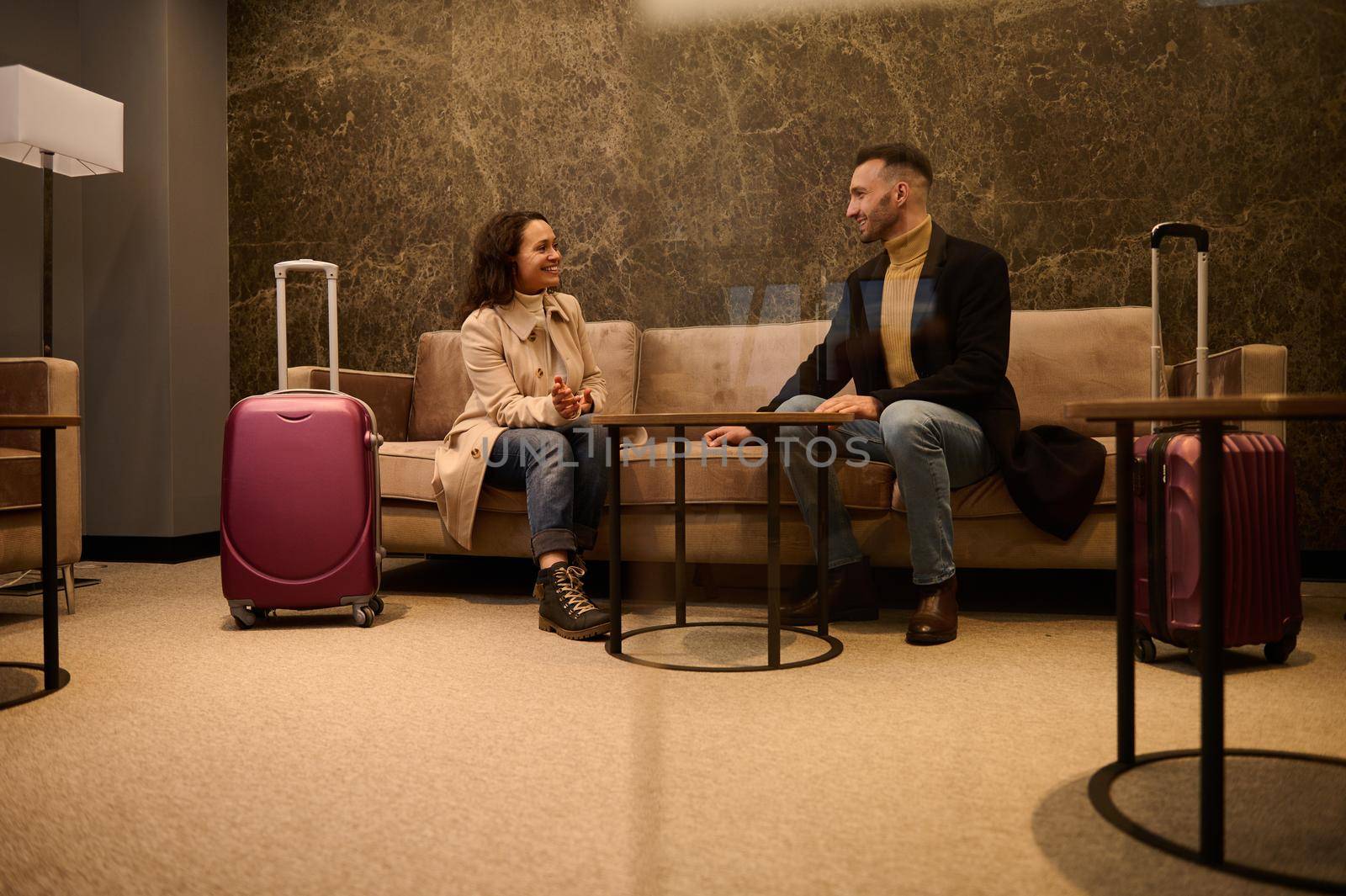Middle-aged handsome man and pretty woman with suitcases, business partners on a business trip having a conversation in a meeting room while waiting for flight in the airport departure terminal