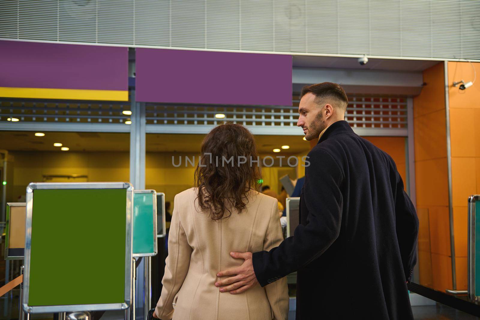 Rear view of a young multiracial couple of business partners standing at the check-in counter while waiting for check-in, customs and passport control at the airport terminal. Copy space