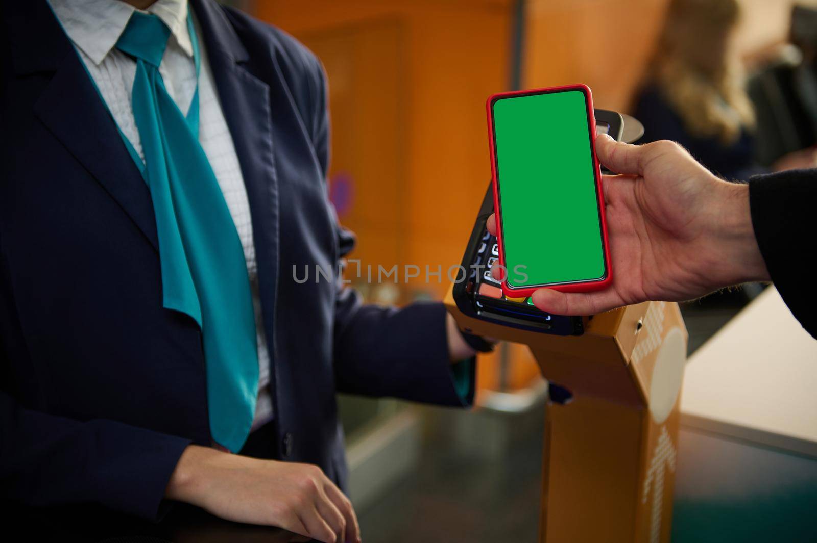 Close-up of man's hand holding mobile phone with green chroma key blank screen with copy space for mobile apps and advertising, near bank terminal while going through flight check-in board at airport