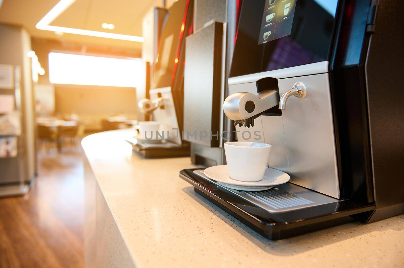 Close-up of professional self-service coffee machines in the restaurant lounge and waiting area of the airport departure terminal. The sun's rays fall indoors at sunset