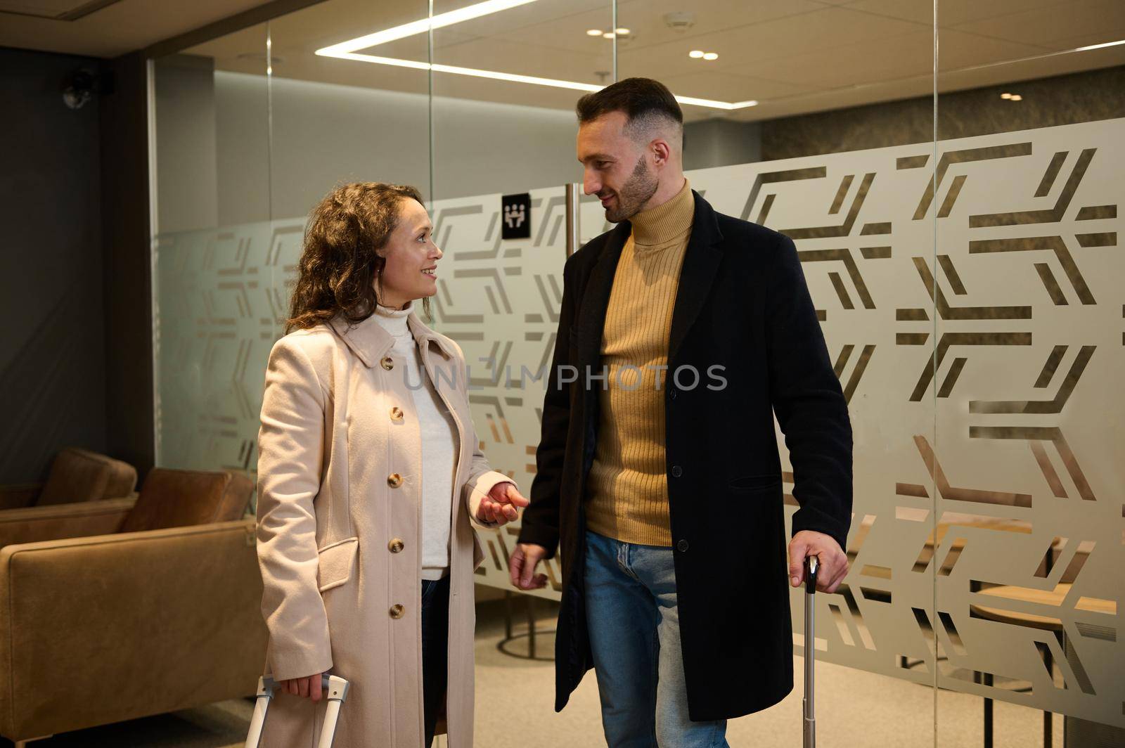 Beautiful Hispanic woman and Caucasian handsome man, multi ethnic couple in love standing at the exit of a VIP room in the airport departure terminal, waiting for flight. Newlyweds at honeymoon trip