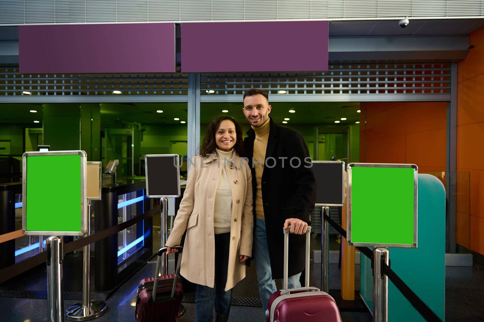 Happy young couple, man and woman, business partners standing with luggage and suitcases at the check-in counter, passing customs and passport control at the departure airport terminal. Copy space