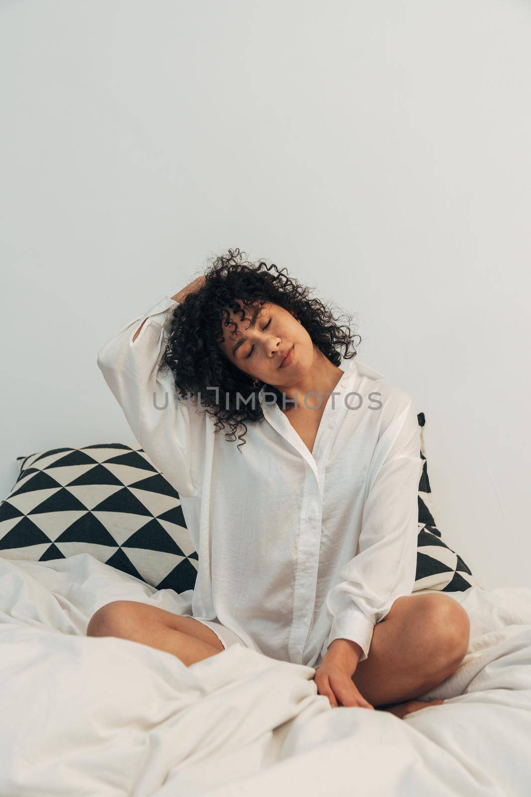 Young mixed race woman stretching neck in bed. Copy space. Vertical image. Healthy lifestyle concept.