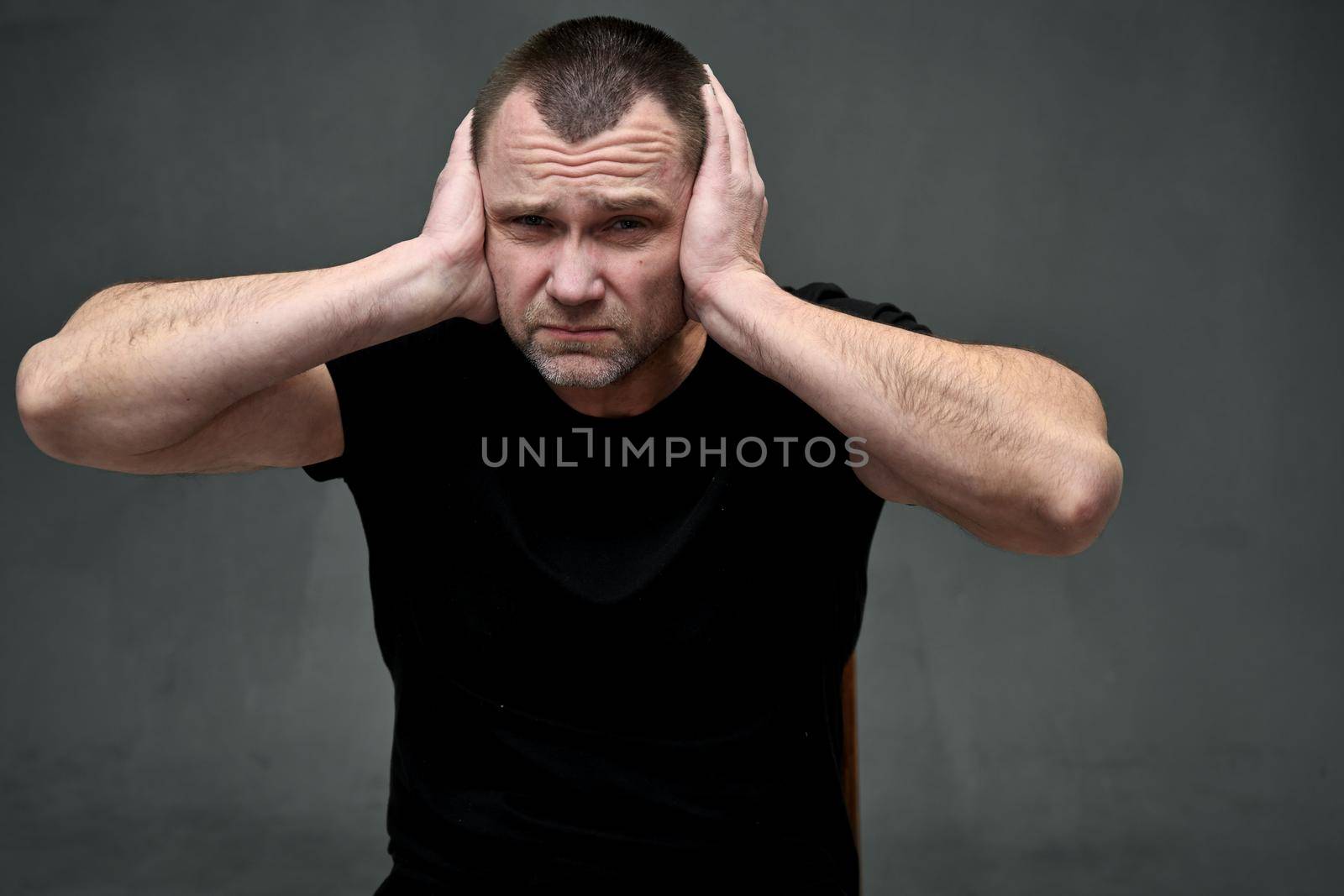 Close-up portrait of a man does not hear, covering his ears with his hands with displeasure