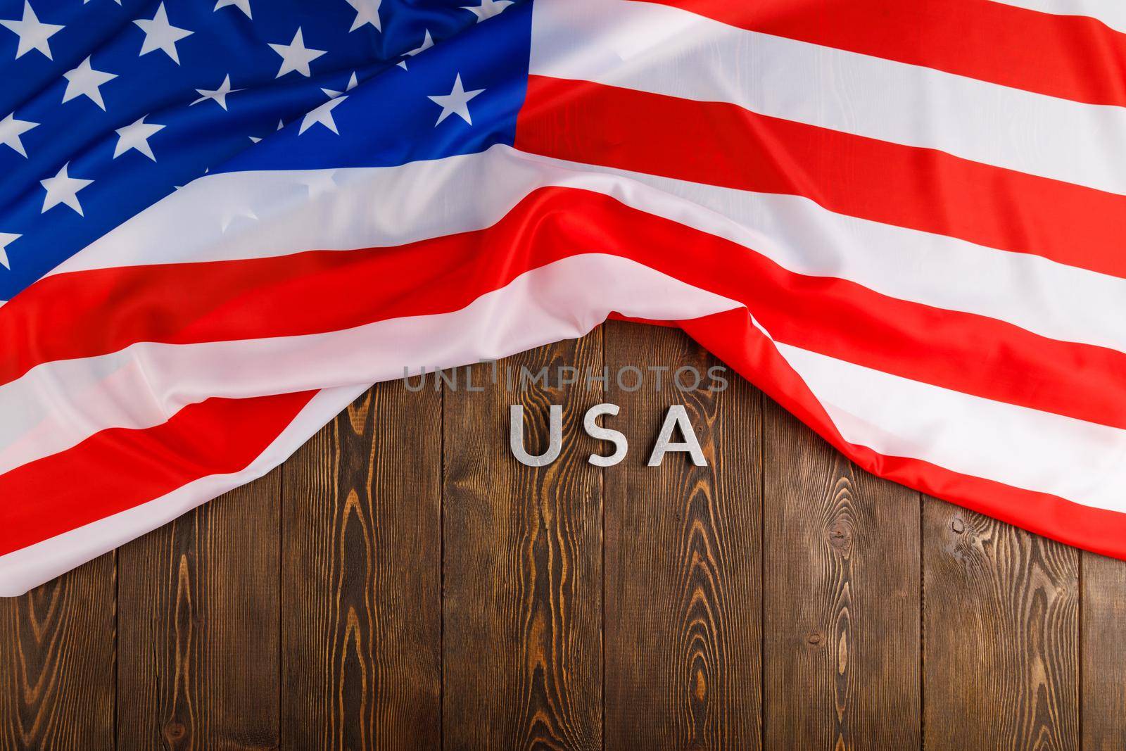 the word USA laid with silver metal letters on wooden board surface under crumpled flag of United States of America in directly above perspective
