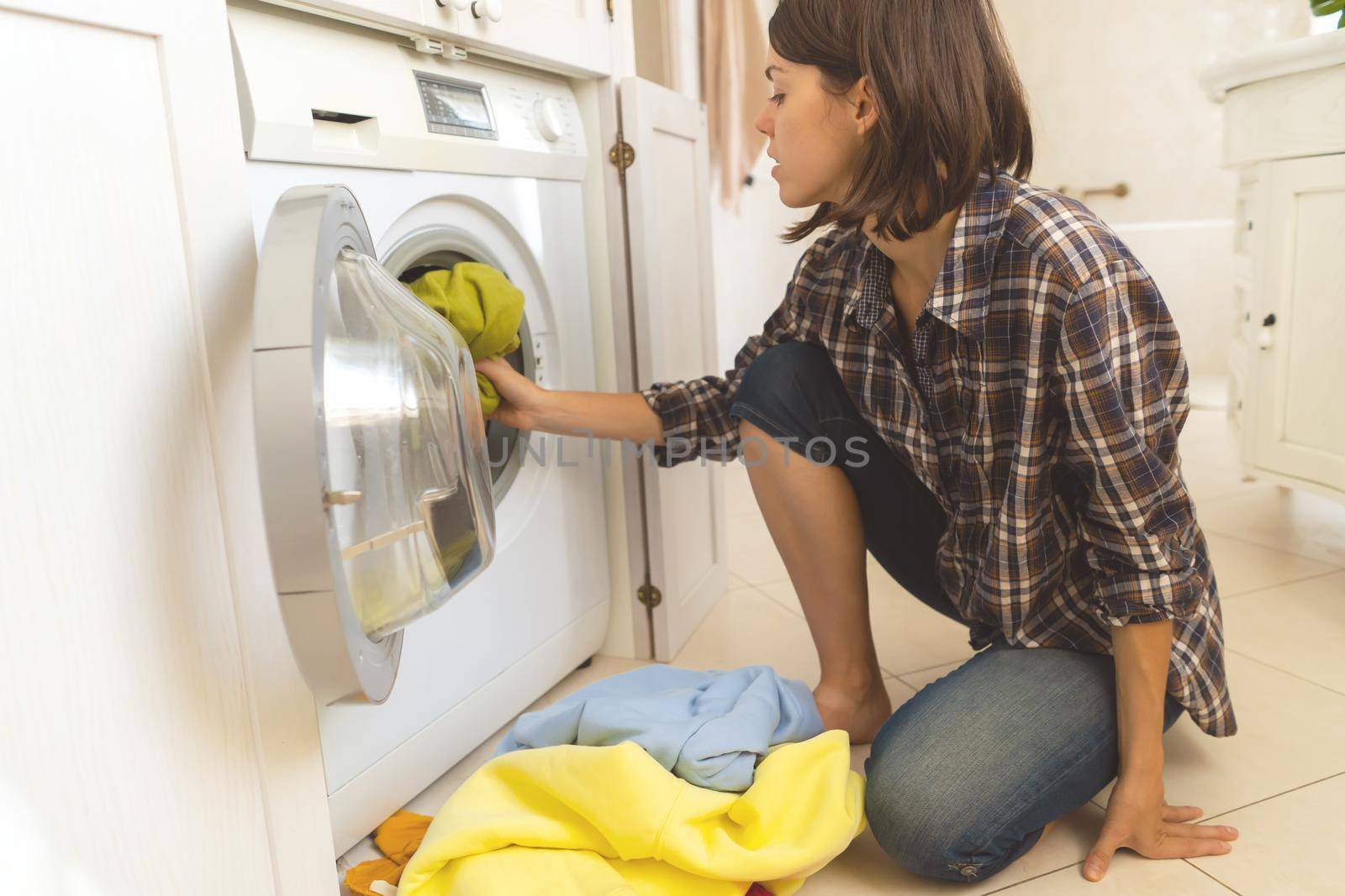 A young girl puts things in the washing machine, a woman sits on the floor of a cozy house and looks at the stain on her jacket, which needs to be removed with detergent.
