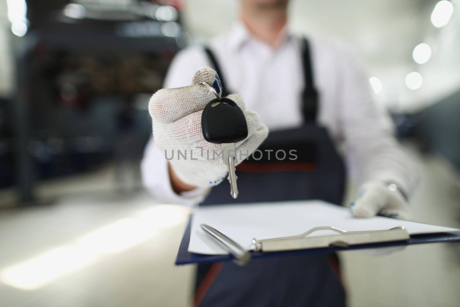 Close-up of service worker give keys from fixed automobile to owner and hold paper for sign. Car service, professional mechanic, garage, pit stop concept