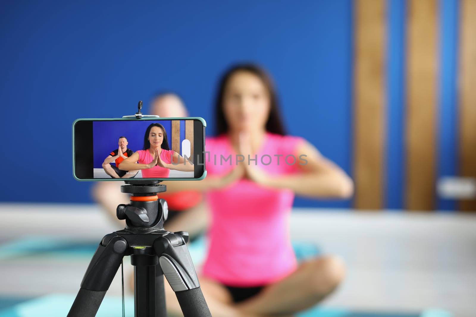 Close-up of camera on tripod filming people perform asana on mat in studio. Morning ritual for body and soul health. Course, social media content concept