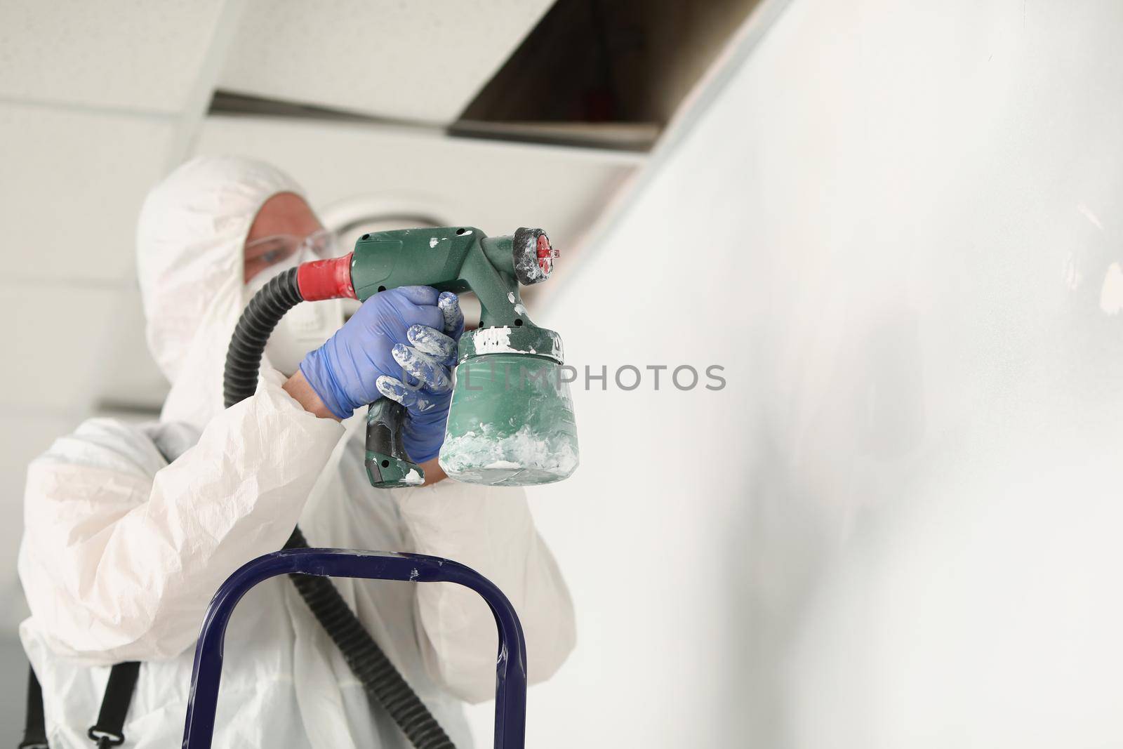 Close-up of male worker painting wall with spray gun in white colour, busy handyman at work. Renovation, construction site, interior, household concept