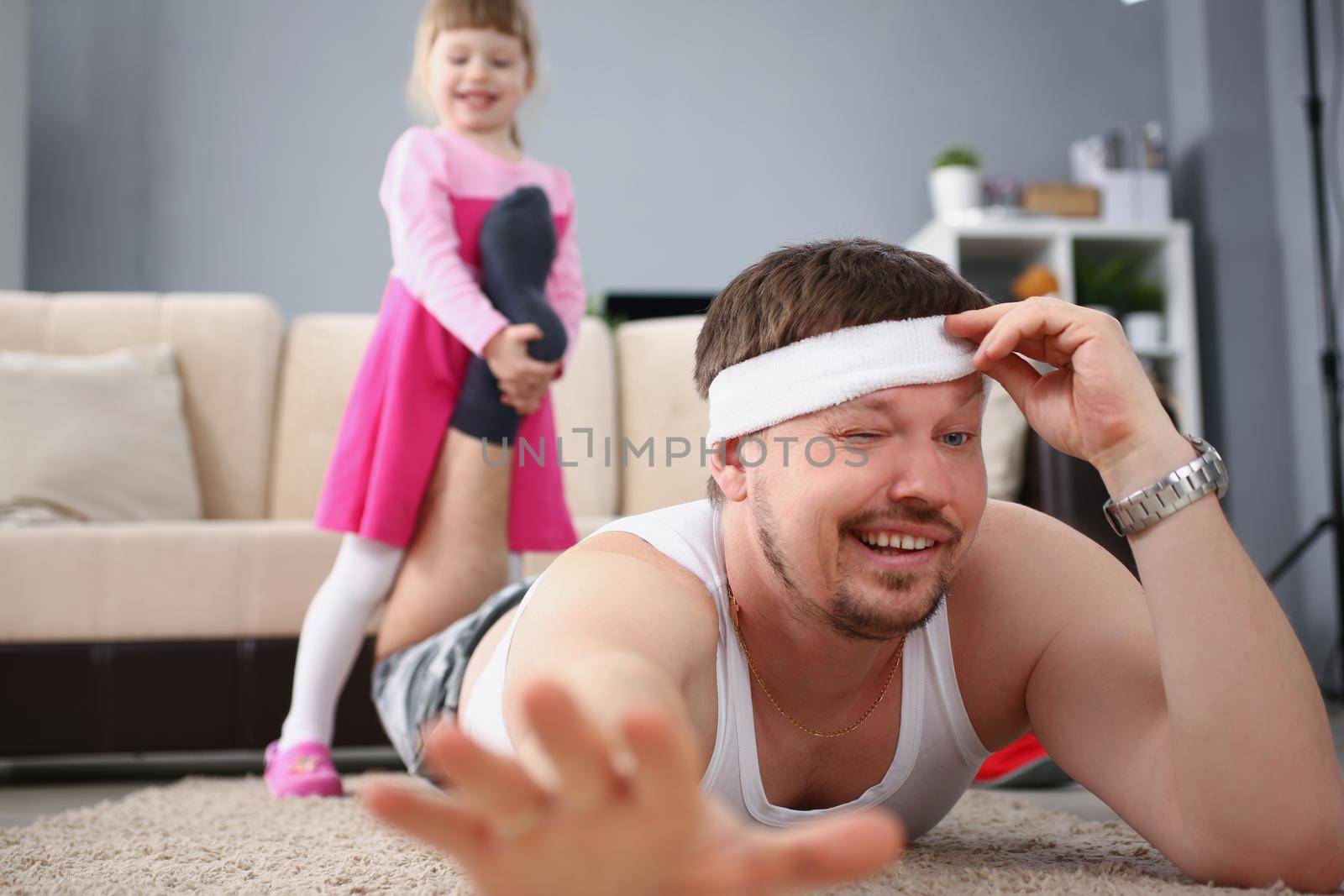 Low angle of girl child pull fathers foot and want to play, tired man lay on floor carpet. Active and happy kid on holiday bored at home. Childhood concept