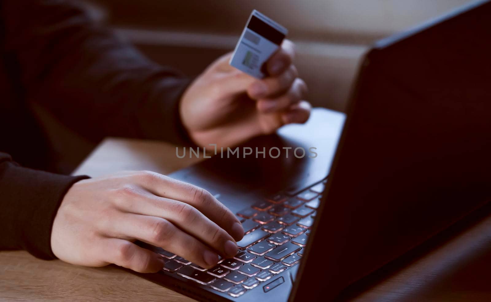 A man holds a bank card in his hand and types on a laptop keyboard, pays for purchases, makes online banking through an application, close-up view of his hands.
