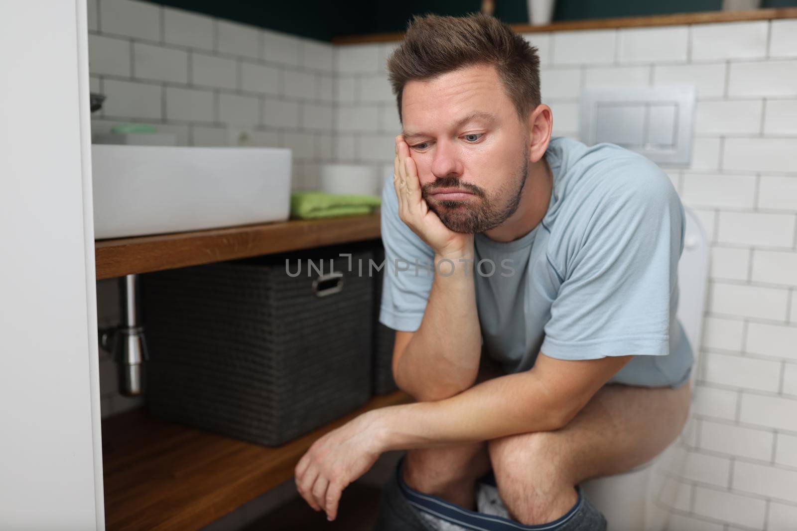 Portrait of bored man on toilet seat dream about something, fulfill natural need, male in bathroom with modern interior. Wc, hygiene, nature calls concept