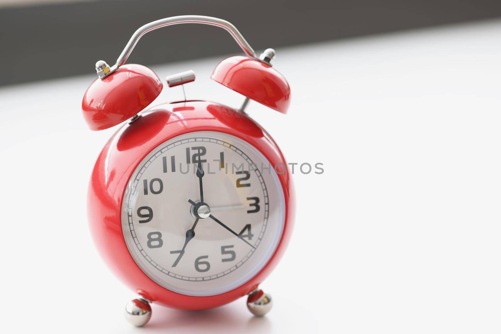 Close-up of retro red clock on white surface show seven in morning, wakeup, time for work. Set alarm for specific time. Vintage, time, late, design concept