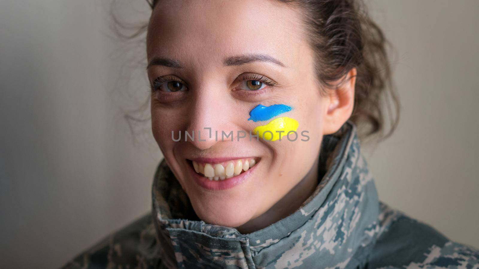 Indoor portrait of young girl with blue and yellow ukrainian flag on her cheek wearing military uniform, mandatory conscription in Ukraine, equality concepts.