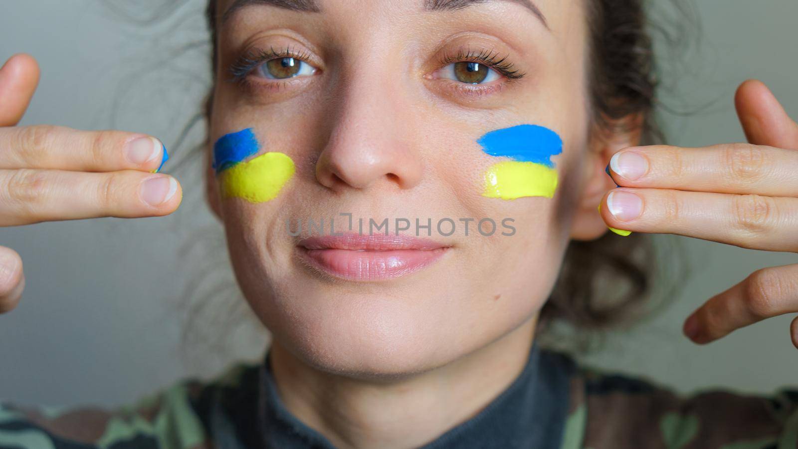 Indoor portrait of young girl with blue and yellow ukrainian flag on her cheek wearing military uniform, mandatory conscription in Ukraine, equality concepts by balinska_lv