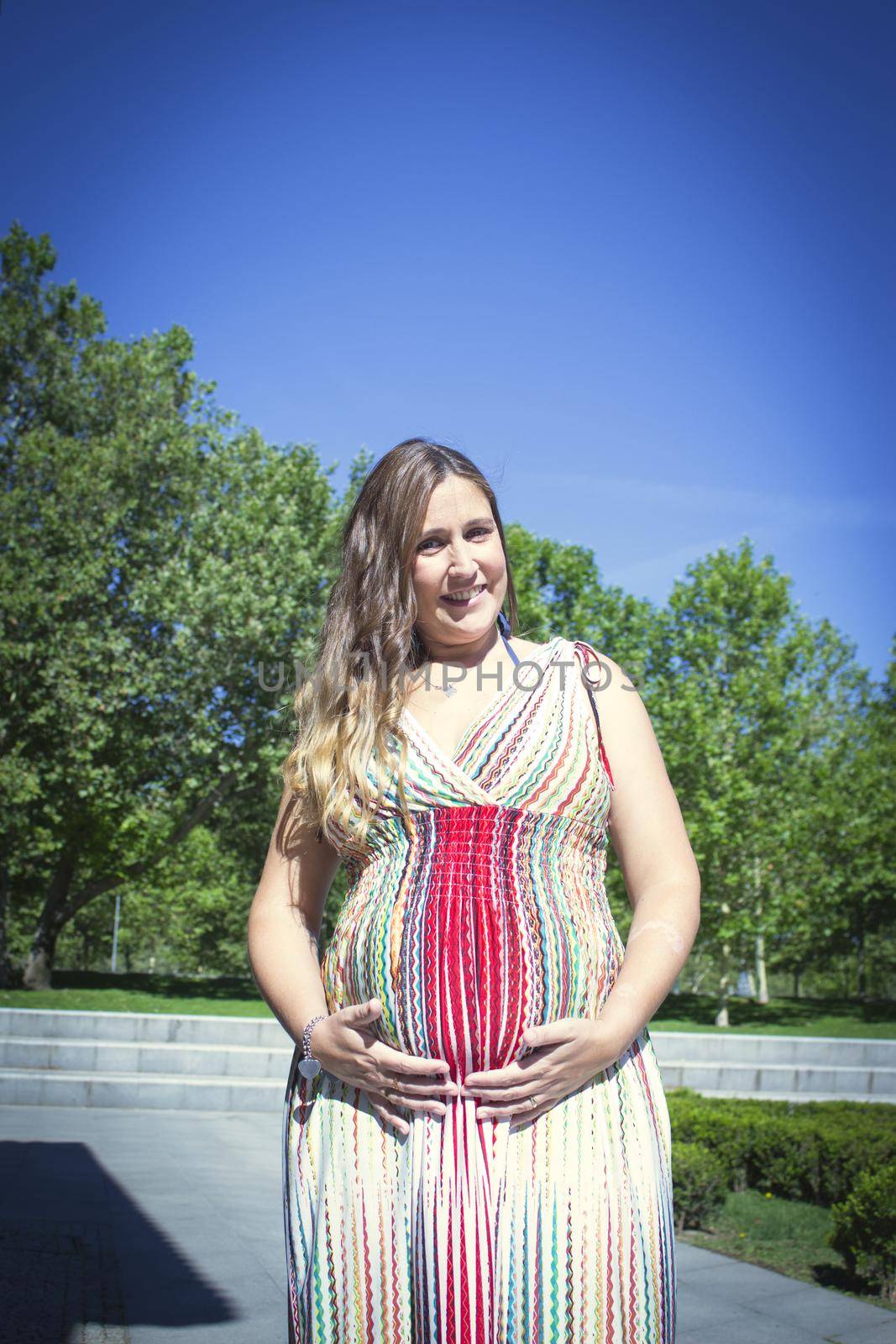 Seven month pregnant woman outdoors in multi colored striped dress by GemaIbarra