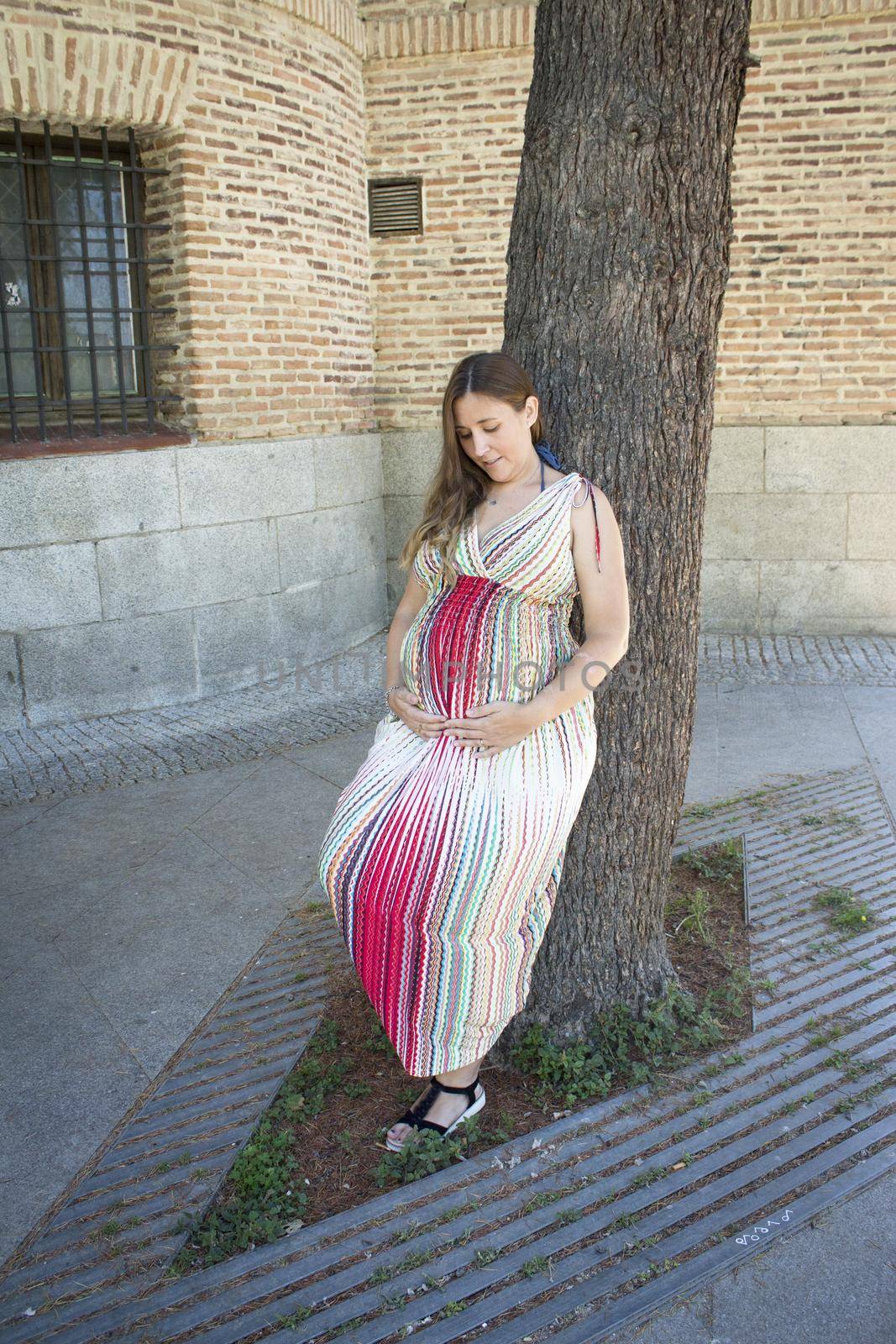 Seven month pregnant woman outdoors in multi colored striped dress. Day scene
