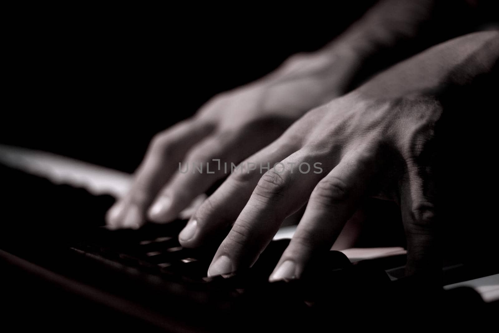 Tattooed mans hands on the keyboard of a piano. Dark background