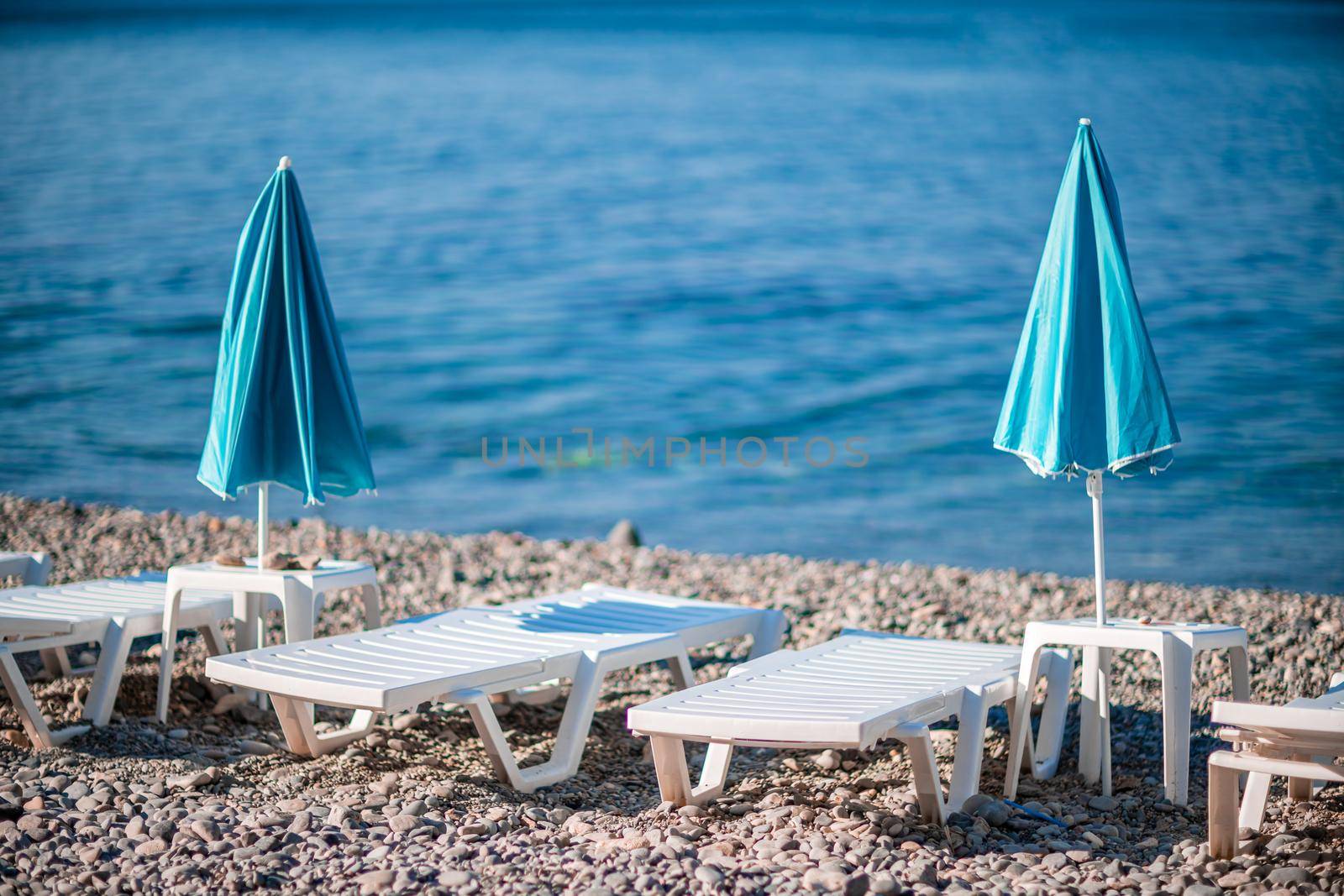 Several white sun loungers and a turquoise parasol on a deserted beach. The perfect vacation concept. by Matiunina