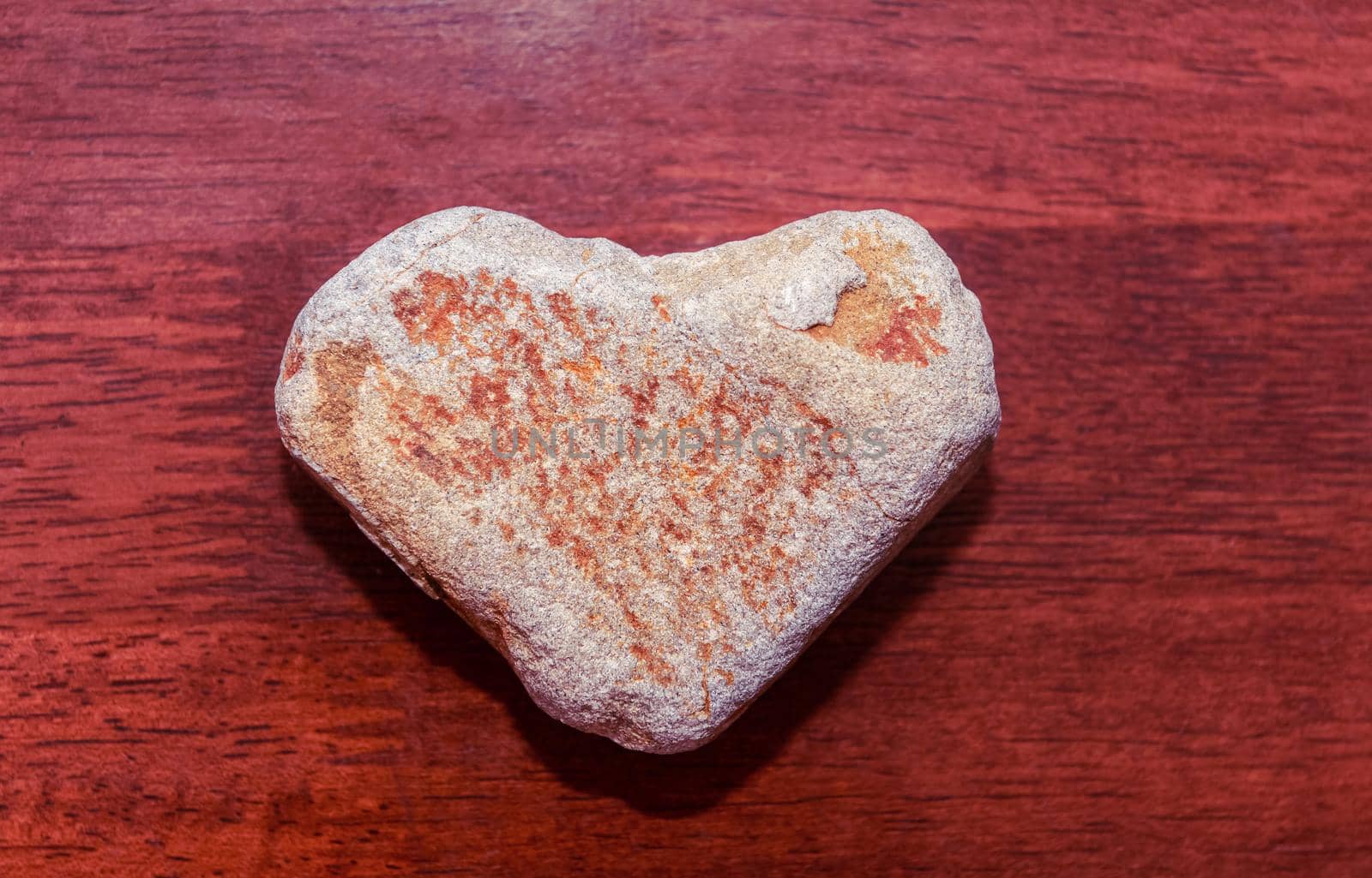 stone shaped like a heart on a wooden surface in red tone. Heart made of natural stone on a wooden background. Valentine's day and holiday concept by karpovkottt