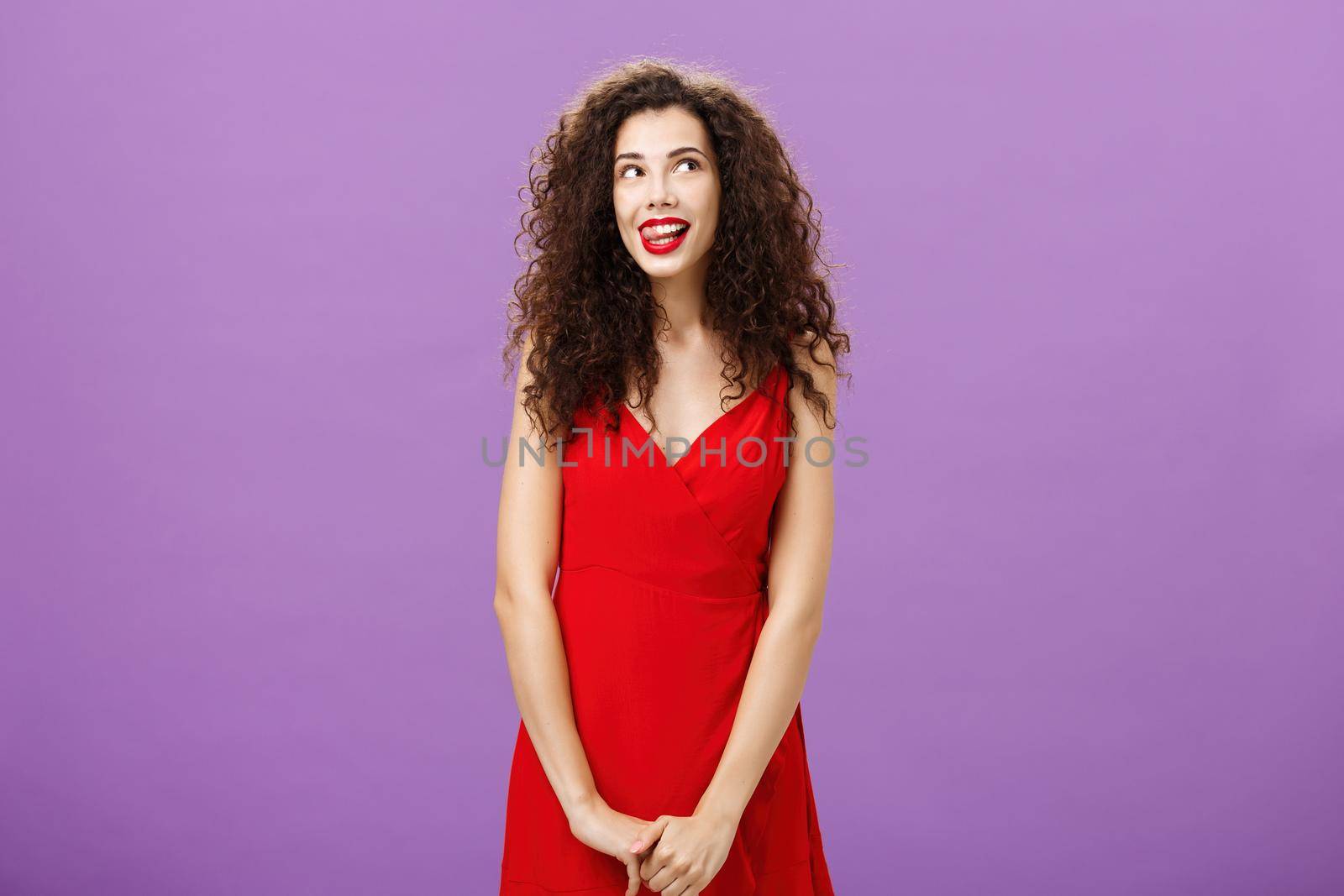 Studio shot of cute thoughtful and creative charming european woman in stylish red licking lips with desire and amusement looking at upper right corner smiling, daydreaming using imagination by Benzoix
