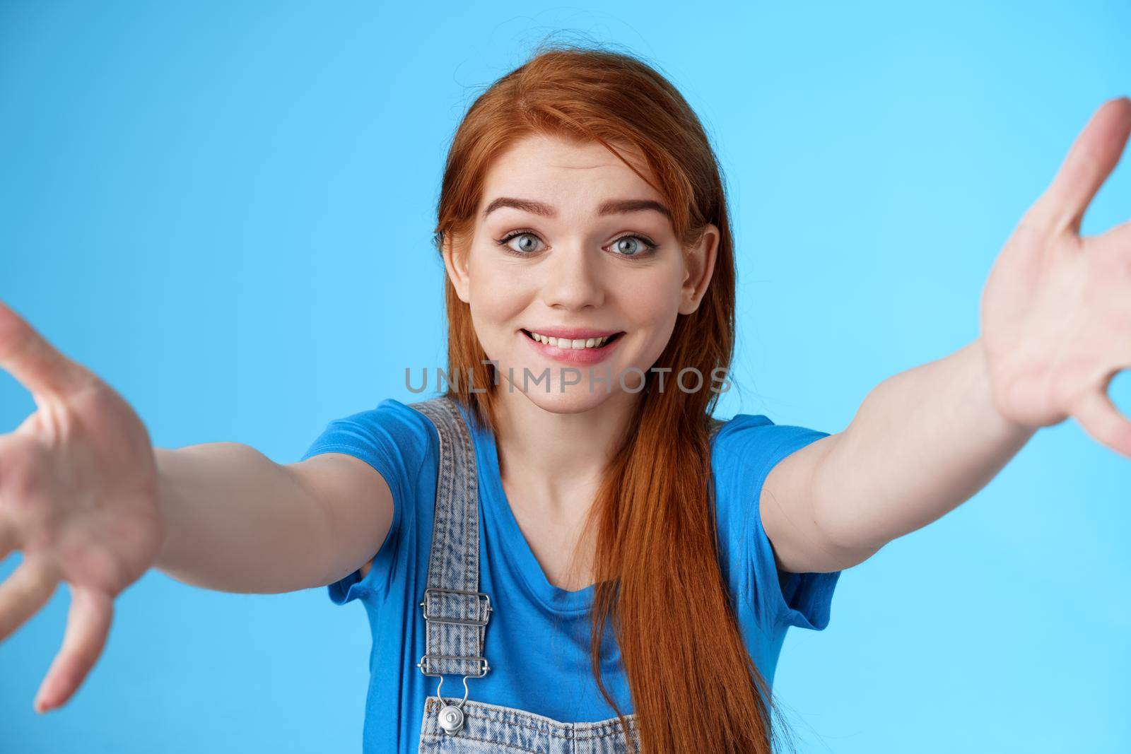 Close-up tender cute supportive redhead girlfriend extend hands waiting you come into arms, catching friend falling, smiling cute sincere, cuddling, friendly hugging, stand blue background joyful.