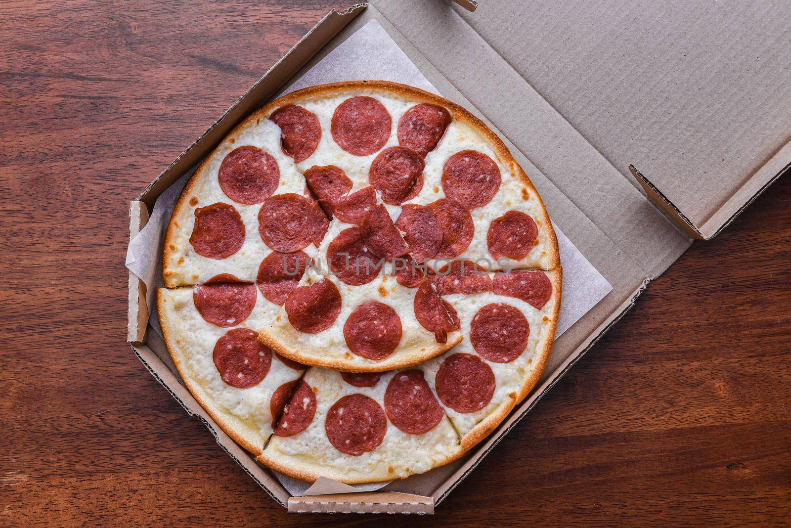 Pepperoni Pizza in open carton box on wooden table, closeup, top view.