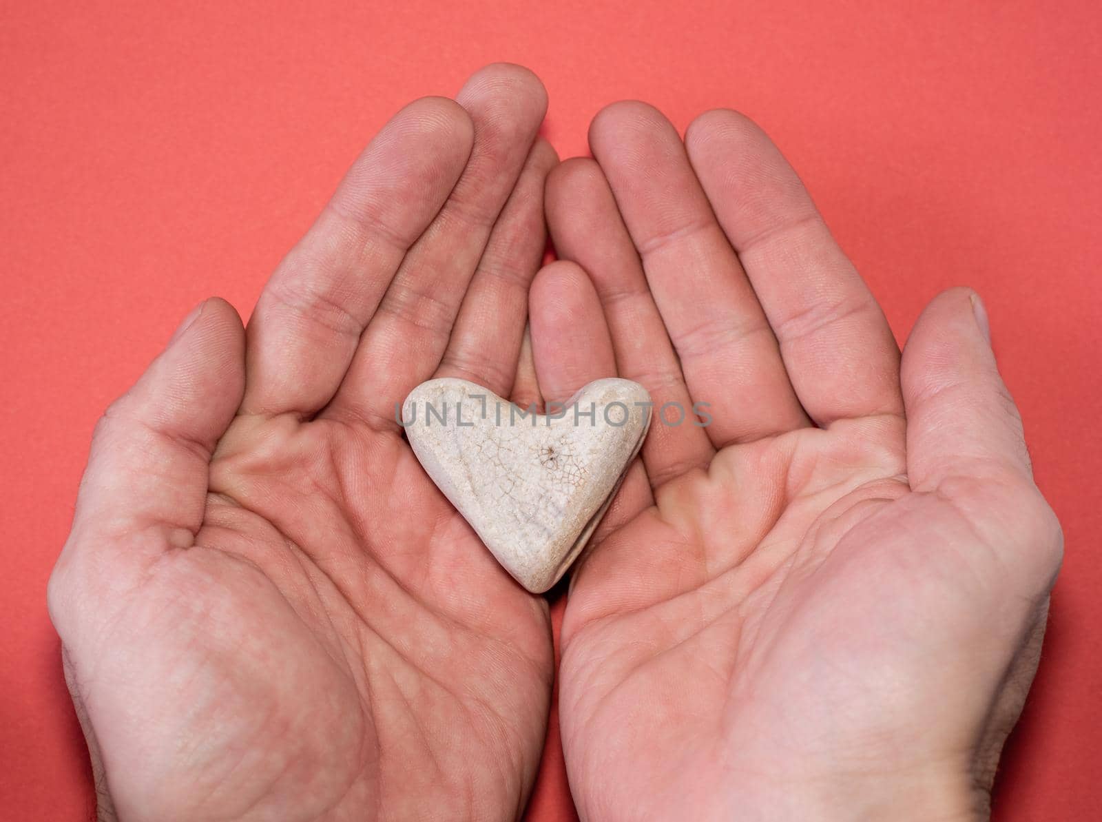 Male hands hold a heart-shaped stone on a red background, close-up. romantic valentine's day gift by karpovkottt