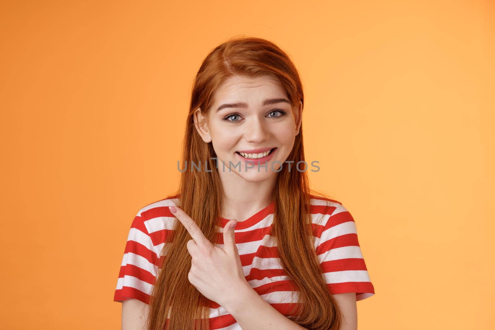 Close-up silly cute redhead female trying help showing way, smiling friendly politely introduce promo, pointing upper left corner smiling modest, stand orange background give advice by Benzoix