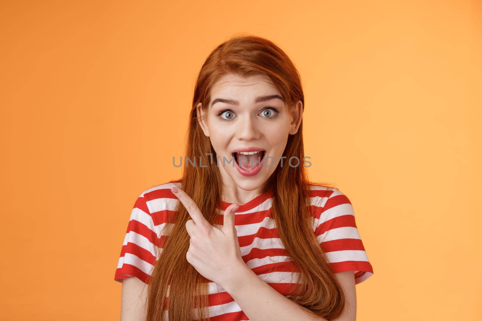Excited female redhead hear impressive sale offer pointing upper left corner, drop jaw astonished stare camera full disbelief surprise, discuss interesting promotion, stand orange background by Benzoix