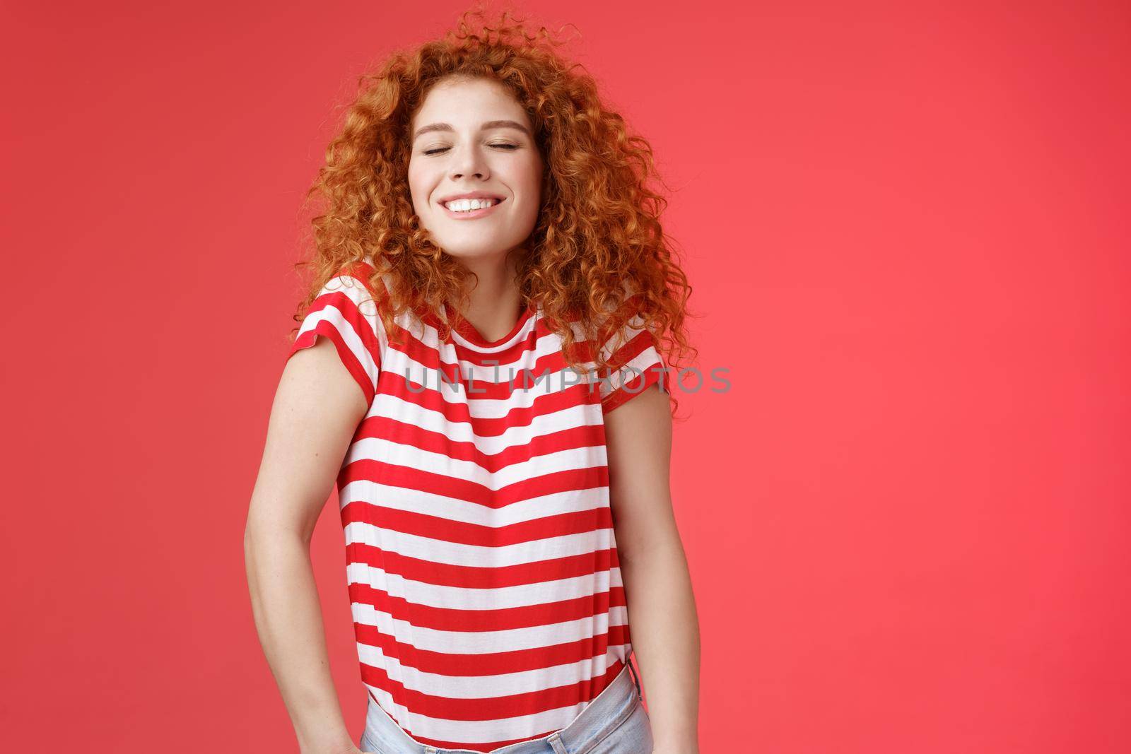 Cheerful relaxed carefree happy attractive redhead curly woman close eyes enjoy sunlight warm summer holiday weekends smiling broadly spend vacation sea trip travel joyfully, red background.