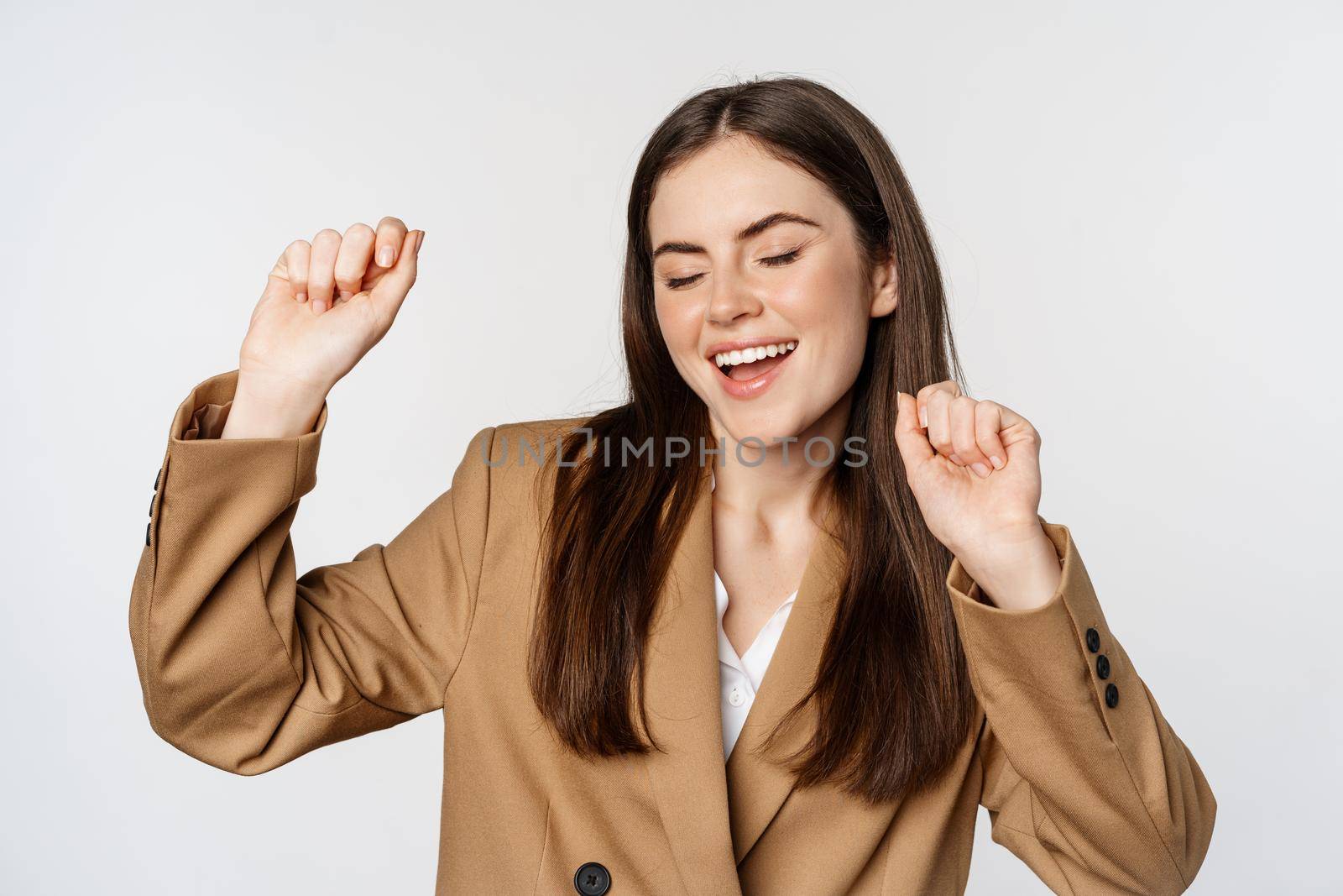 Successful businesswoman, saleswoman dancing and having fun, wearing office suit, posing over white background.