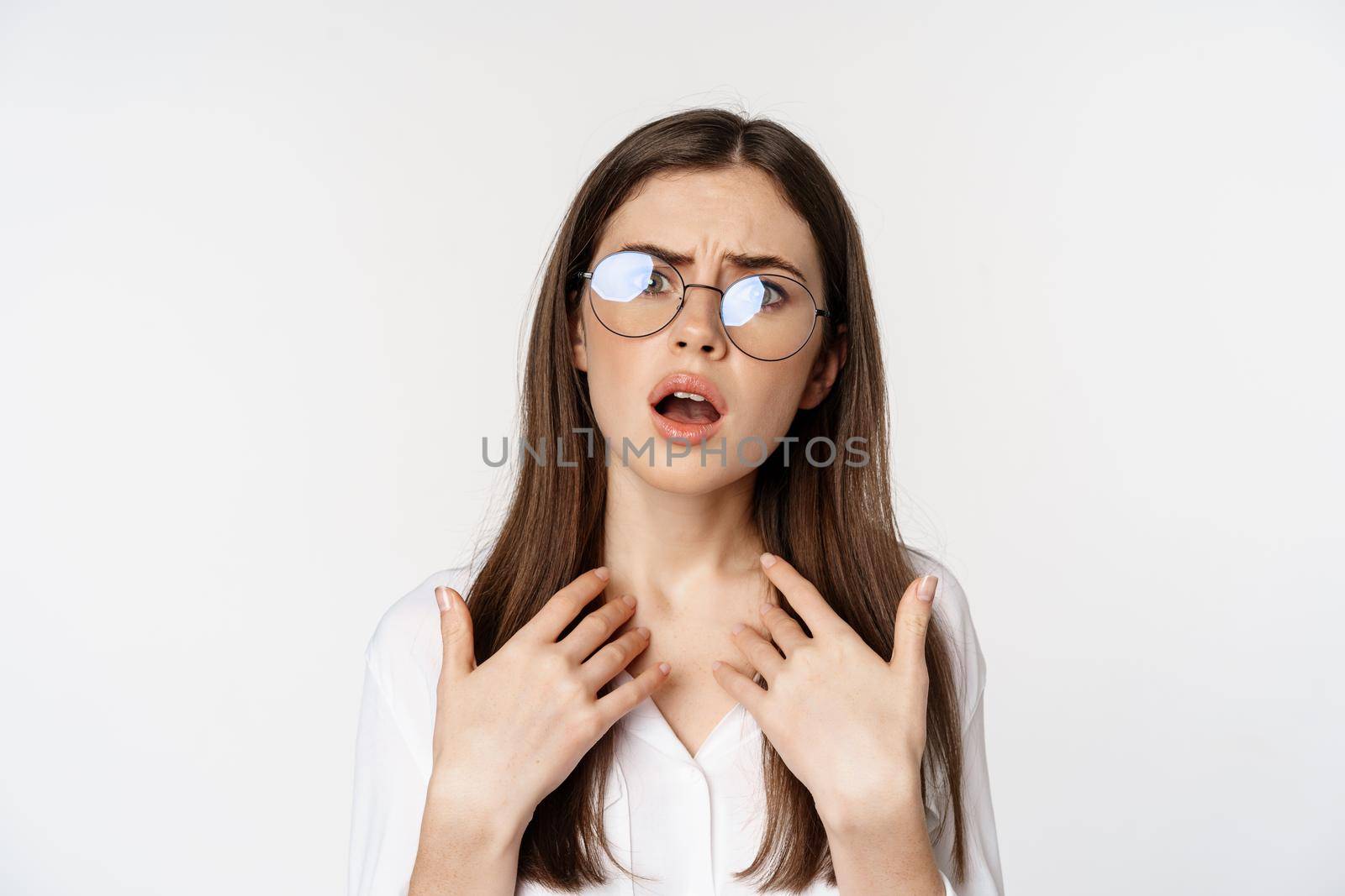 Offended and upset young woman in glasses, beeing jealous or disappointed, feeling hurt, grimacing and sulking, standing confused over white background.