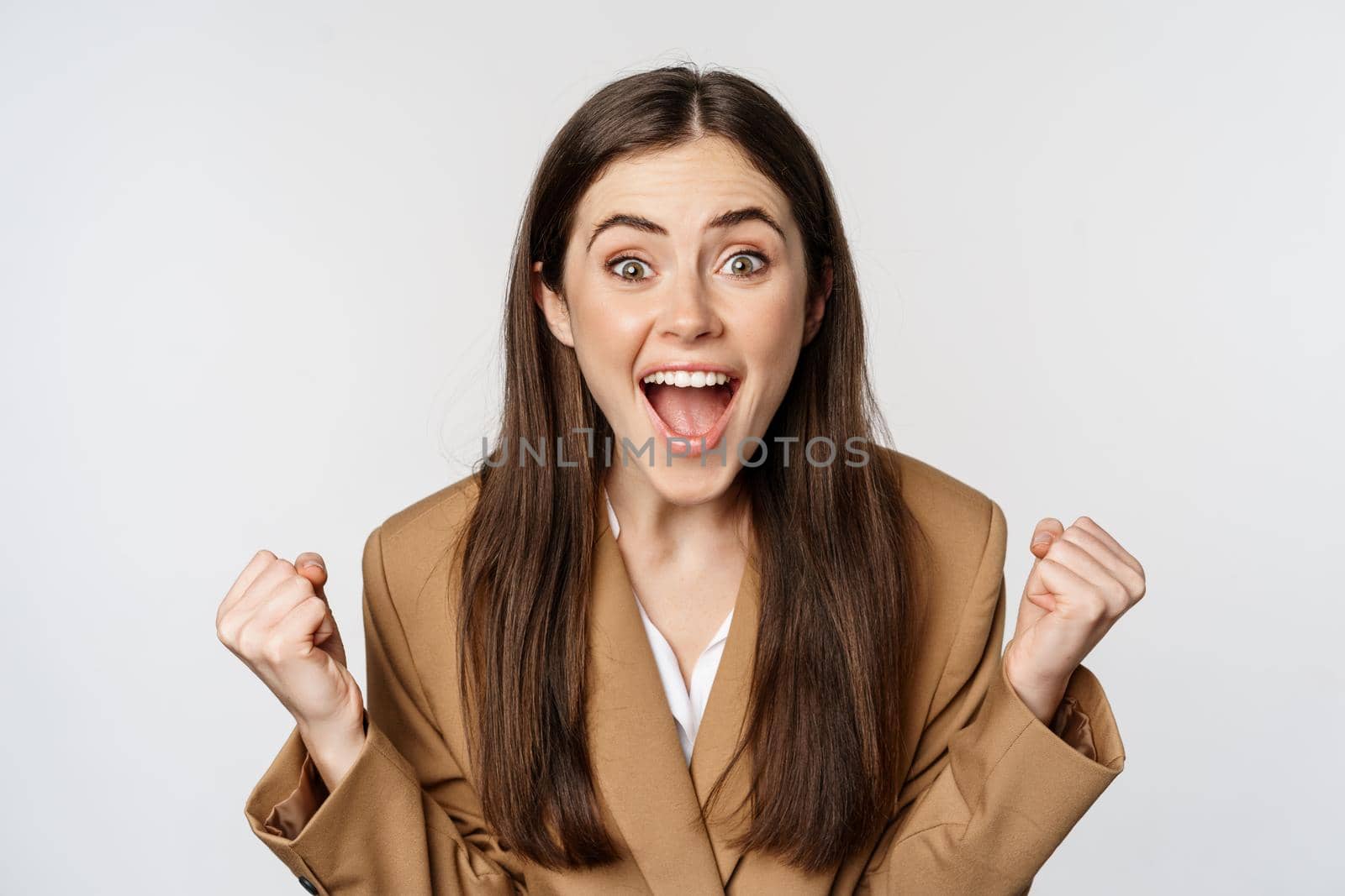 Enthusiastic girl screaming and rejoicing, looking at camera, winning, celebrating victory and triumphing, standing over white background.