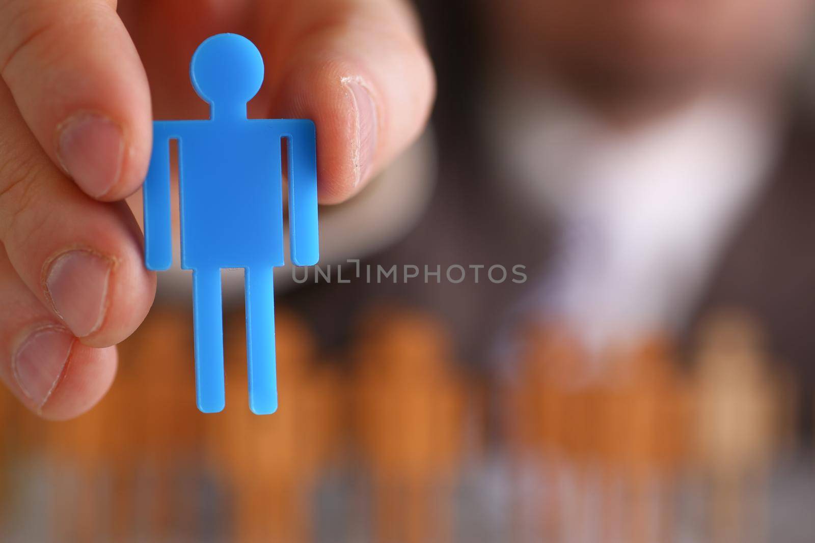 Man hand holds blue plastic human figurine. Employee selection and search concept