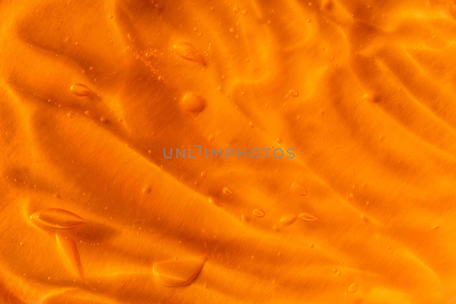 Texture of transparent yellow gel with air bubbles and waves on orange background. Concept of skin moisturizing, body care and prevention of covid19. Liquid beauty product closeup. Backdrop, flat lay