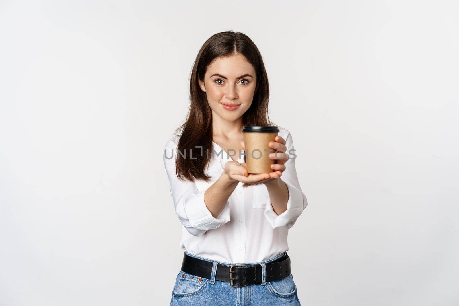 Image of modern woman, office lady holding takeaway coffee cup and smiling, standing over white background.