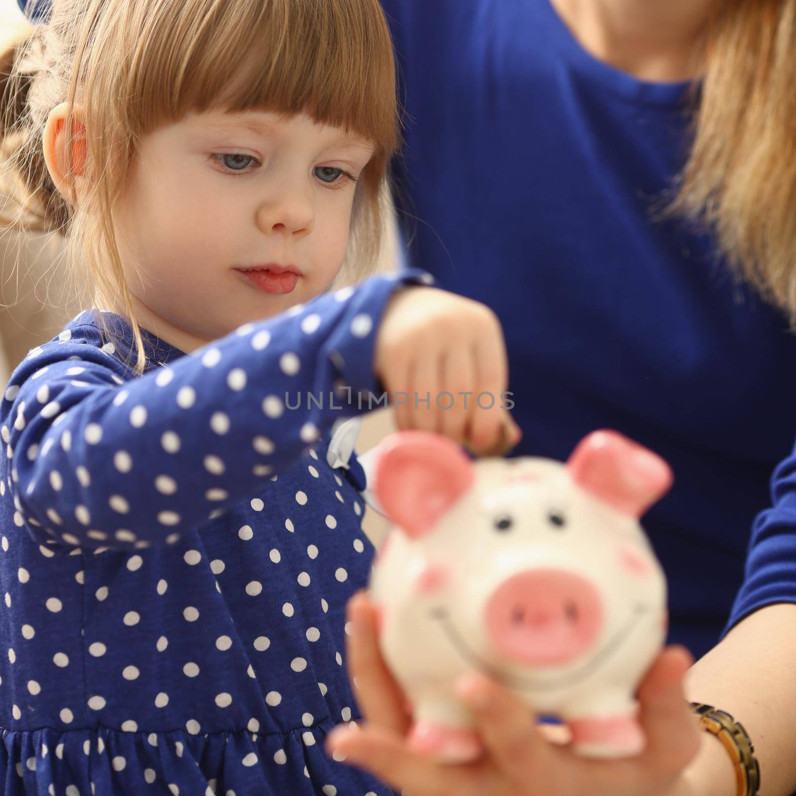 Little child girl with mom throws coins into piggy bank. Family budget and financial expenses planning concept
