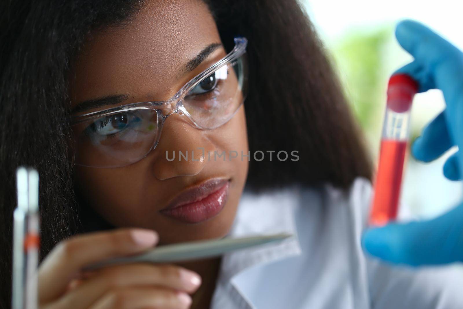 African american chemist holds glass test tube with red liquid solution. Analyzing various reagent options using a chemical manufacturing concept